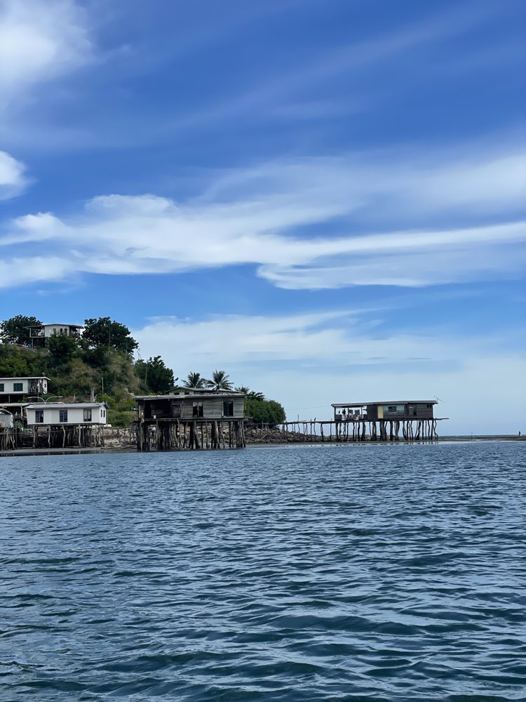 Houses on stilts over the water at Barakau Village, under a wide blue sky