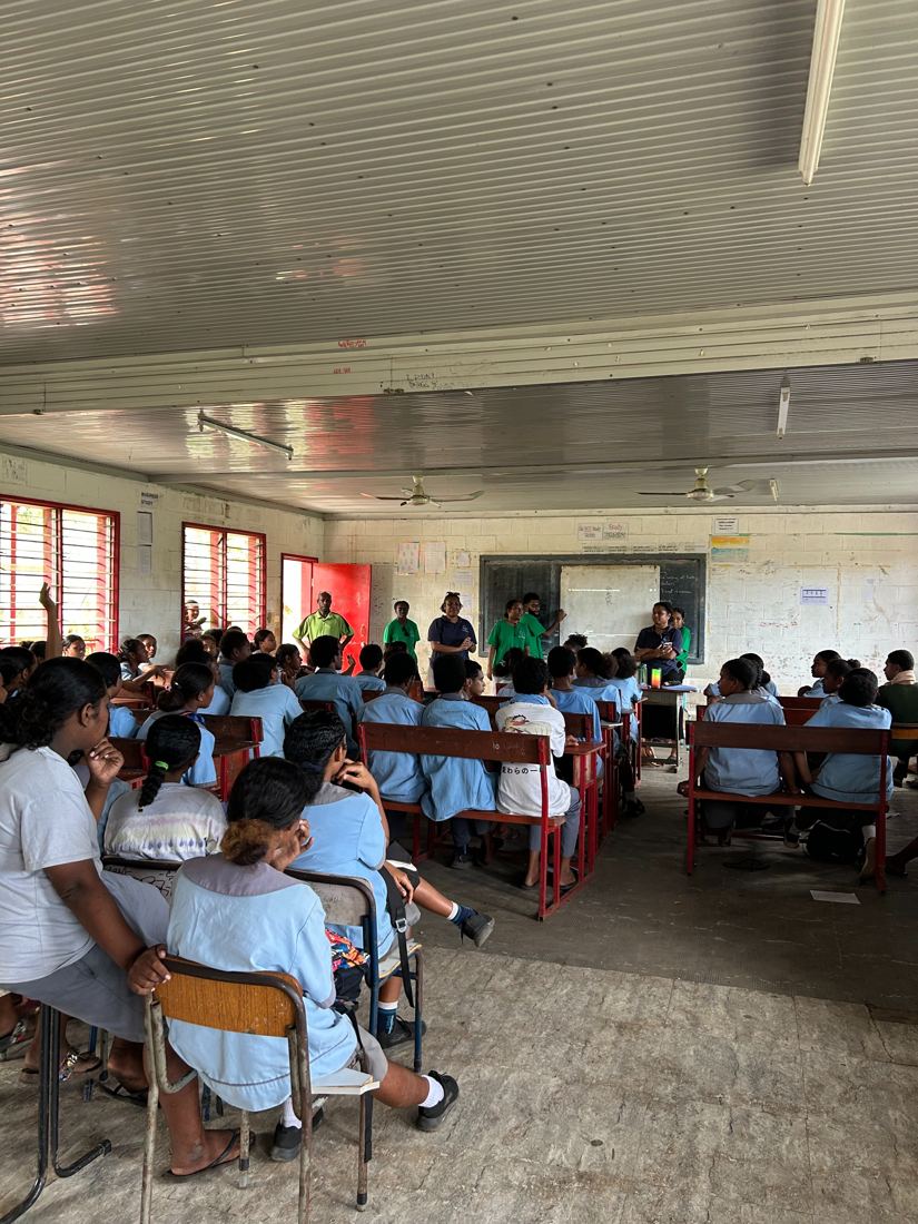 Eda Davara team presenting to a full classroom of students in blue uniforms