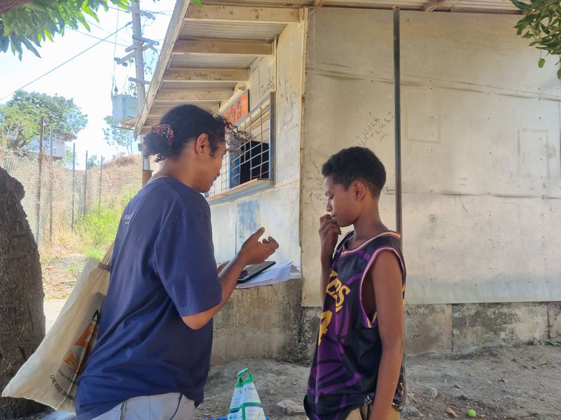 An EcoScholar interviewing a young community member with a tablet and survey forms