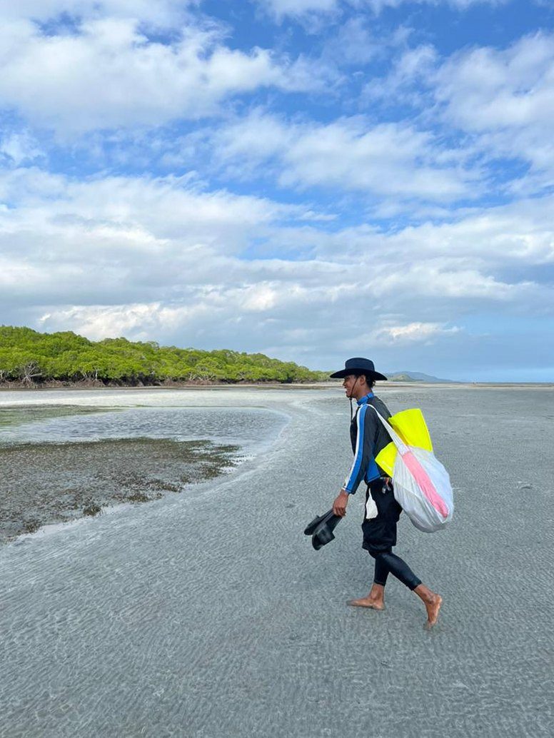 Ulato Manau, Community Field Assistant, walking across the Kohua tidal flats with survey gear