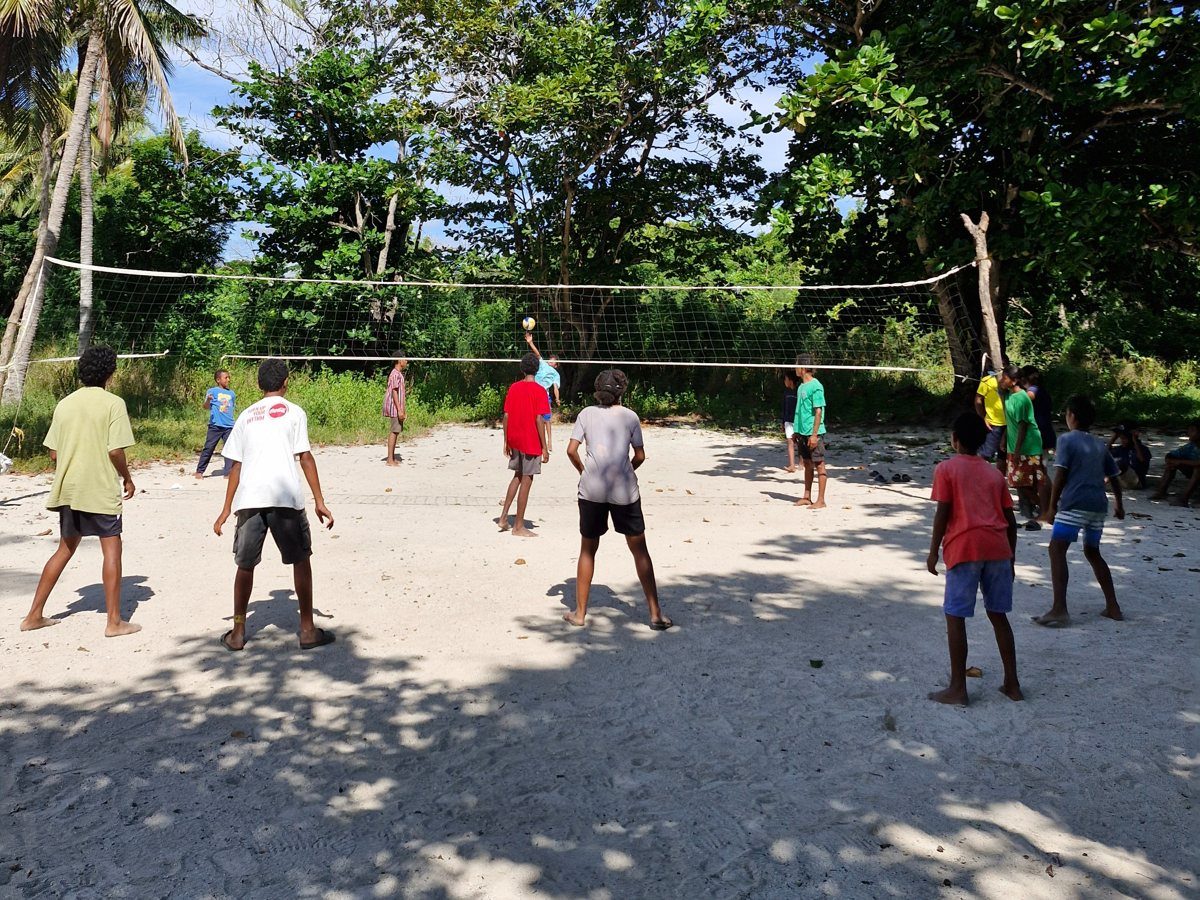 Young people playing volleyball on the sand court under the trees at Kohua Beach